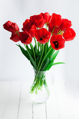 Glass vase with red tulips on wood table
