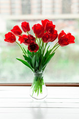 Red tulips bouquet in glass vase on wood