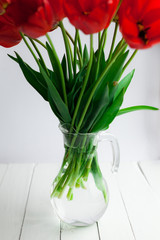 Red tulips bouquet in glass vase on wood table, selective focus