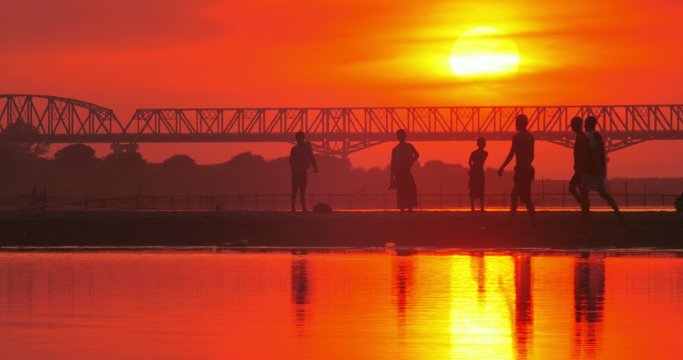 Silhouettes of people playing soccer on shore of Irrawaddy river and red sunset
