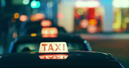 Close up view of taxi sign on roof of the cab moving on street at night.