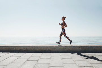 Jogging athlete young woman running at sea background.