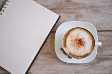Open a blank white notebook, pen and cup of coffee on the desk