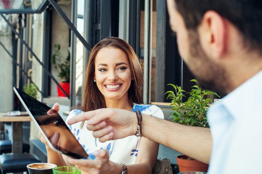 Young Couple In Sidewalk Cafe And Using Digital Tablet.