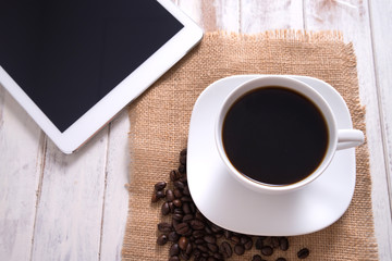Cup of hot coffee and tablet on wood table background