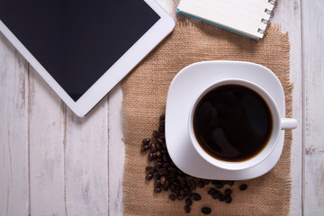 Cup of hot coffee and white note book on wood table background