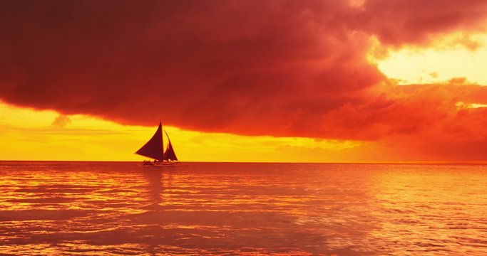 Vivid orange sky at sunset on coast of tropical sea with sail boats on horizon. 