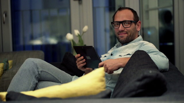 Portrait of happy man with tablet computer sitting on sofa at home
