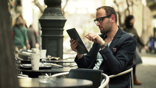 Young man using tablet computer while sitting in cafe in city
