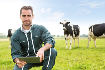 Portrait of a young attractive farmer in a pasture with cows