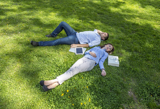Young man and woman napping on grassy lawn.
Cute young man and woman casual dress official shirt napping dreaming lie on green grass with yellow flowers laptop tablet PC book around