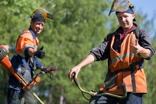 Smiling landscapers during grass cutting team works with string trimmers gesturing ok