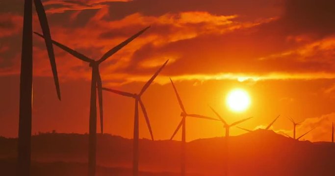 Many wind mills turbines power generators at sunset with colorful clouds