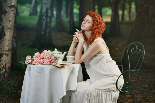 Beautiful redhead woman having tea in the forest