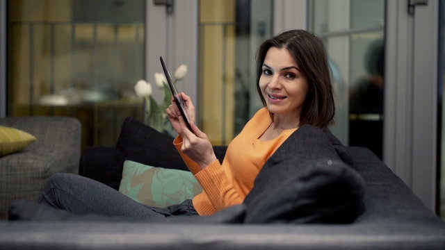 Portrait of happy woman with tablet computer sitting on sofa at home
