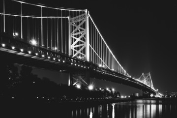 Fototapeta na wymiar Black and white photo of the Benjamin Franklin Bridge at night,
