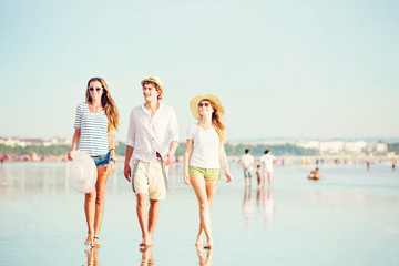 Group of happy young people walking along the beach on beautiful