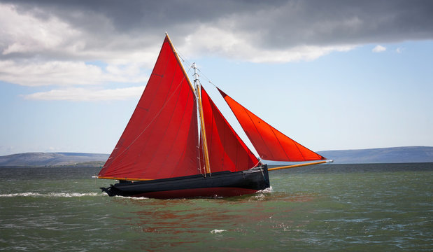 Traditional wooden boat with read sail.