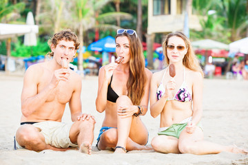 Group of happy young people eating ice cream on the beach