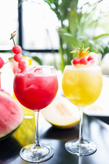 mix of refreshing glass of bright juicy melon and watermalon smoothie or lemonade with ice on a table at a restaurant with the decor of the bright dishes and pieces of melon