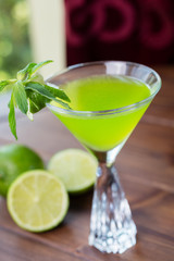 refreshing glass of cold lime lemonade with mint on a wooden table in a restaurant with a creative decoration of mint leaves and fresh lime. soft focus