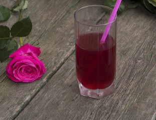 glass of red drink with a tubule nearby a rose