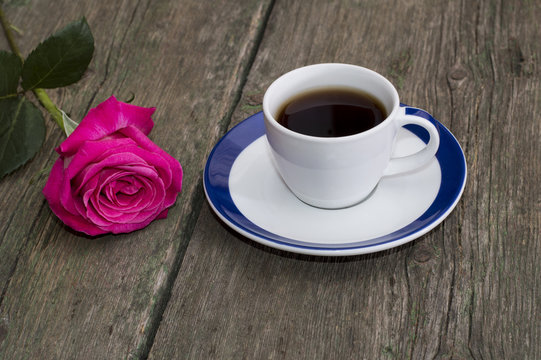cup of coffee on an old table and nearby a rose