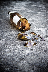 Shattered brown beer bottle resting on the ground: alcoholism co