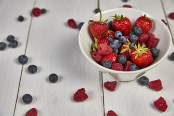 Different berries in a white bowl on a white wooden table