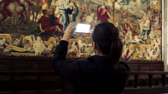 Woman taking photo of fresco with cellphone in church
