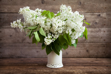 Still life. Bouquet of white lilacs in a vase on a wooden table.