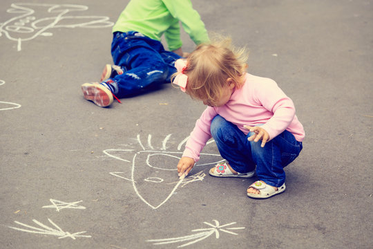 two little kids drawing on asphalt outdoors