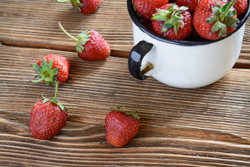 Strawberries in white old metal cup on wooden rustic background
