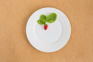 клубника с листьями салата на белой тарелке сверху