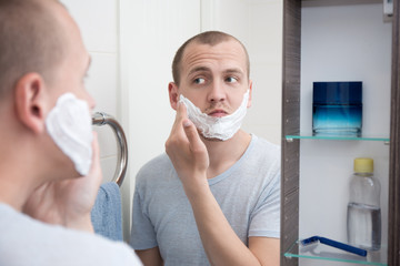handsome young man applying shaving foam to his face