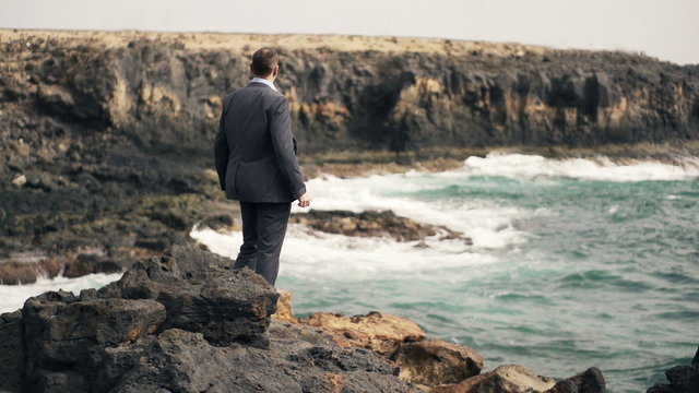 Young businessman looking at sea while standing on rocks, slow motion shot at 240fps
