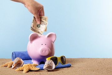 Hand putting US American dollar into a Piggy Bank or piggybank standing on a sunny tropical beach...