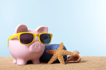 Piggy Bank or piggybank wearing sunglasses standing on a sunny tropical beach with towel holiday...