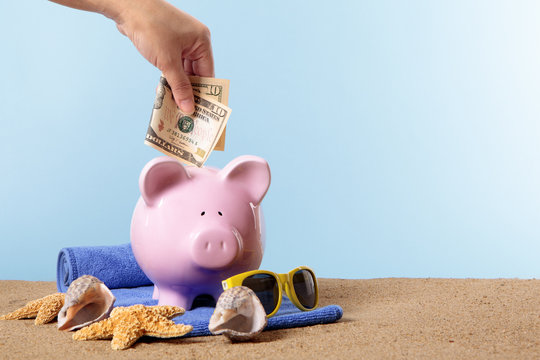 Hand putting US American dollar into a Piggy Bank or piggybank standing on a sunny tropical beach with towel holiday vacation retirement saving money plan photo