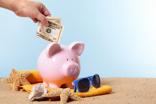 Hand putting US American dollar into a Piggy Bank or piggybank standing on a sunny tropical beach with towel holiday vacation retirement saving money plan photo