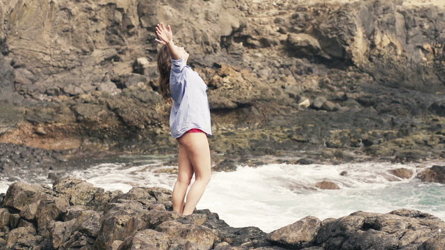 Happy woman in mens shirt enjoying herself standing on rocks near sea, slow motion shot at 240fps 
