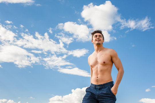 Fit young man with bare torso standing under scenic blue sky on sunny day