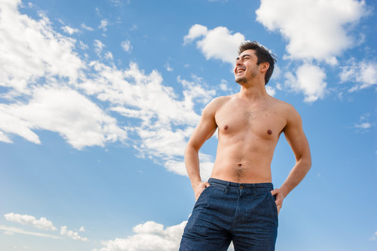 Fit young man with bare torso standing under scenic blue sky on sunny day