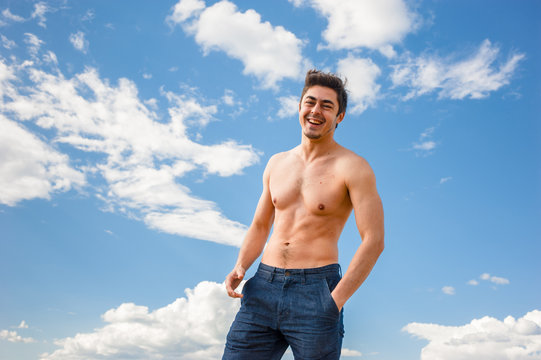 Fit young man with bare torso standing under scenic blue sky on sunny day
