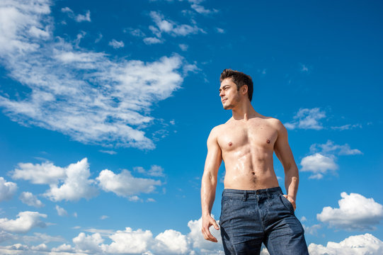 Fit young man with bare torso standing under scenic blue sky on sunny day
