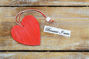 Because I care card with red wooden heart on rustic surface
