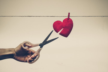 hand with scissors trying to cut a red heart on a rope