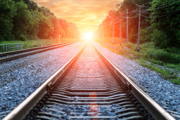 Fototapeta na wymiar Straight Railroad into orange sunset with clouds in sky