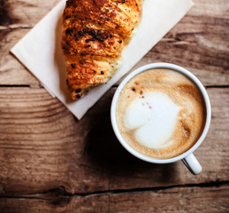 Coffee and fresh croissant for breakfast on rustic wooden table,