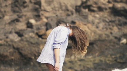 Young woman in mens shirt throwing her hair while standing on rocks near sea, slow motion shot at 480fps 

